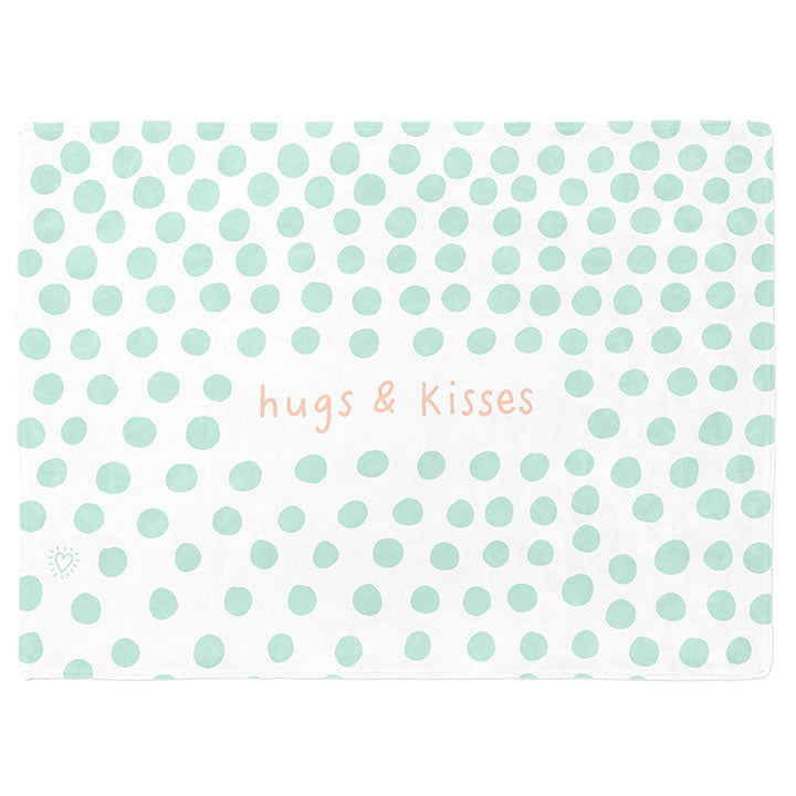 30 by 40 inch silky-soft fleece blanket that is hypoallergenic. Perfect size for a toddler or child. Bright white blanket printed on one side only. 3 inch hand drawn mint green dots scattered across blanket with the words hugs & kisses hand drawn in a peach color. A small Adoptionly Yours heart logo by itself in mint green in lower left corner of blanket on front. 