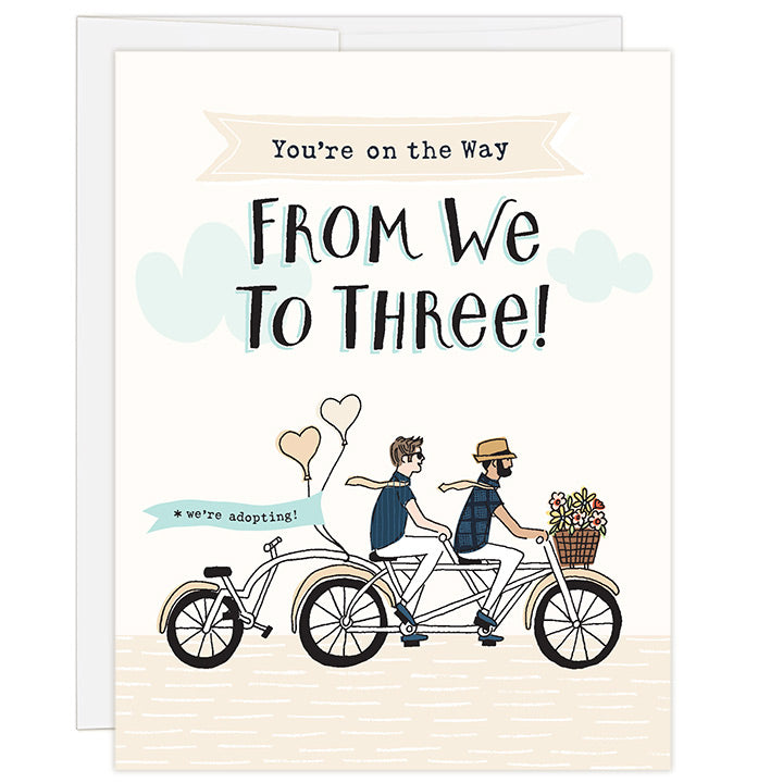4.25 x 5.5 inch greeting card. Blank inside. Simple and charming illustration style. Title You’re on the Way From We to Three! Sub title *we’re adopting! Main image is two men on a tandem bicycle, both with neck ties that are blowing in the wind and a third wheel back seat is empty. There are flowers in the basket and balloons on the back with the words we’re adopting!