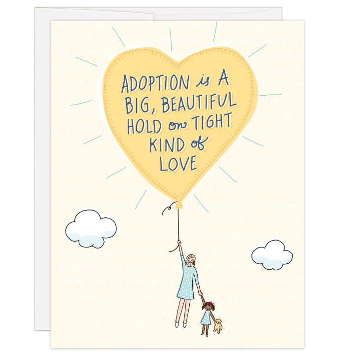 4.25 x 5.5 inch greeting card. Blank inside.  Cover art is a bright yellow balloon lifting up a caucasian mother and African American child, child holding a teddy bear all on cream background. Hand-illustrated text reads: Adoption is a big, beautiful hold on tight kind of love. 
