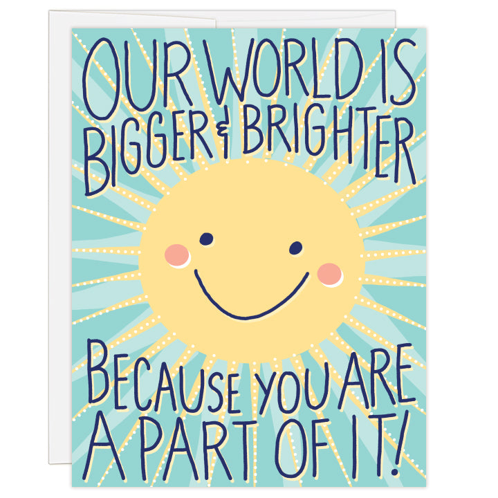 4.25 x 5.5 inch greeting card. Blank inside.  Illustrated cover art is a bright yellow sun with smiling face on a teal background with artful sun rays. Text: Our world is bigger and brighter because you are a part of it!