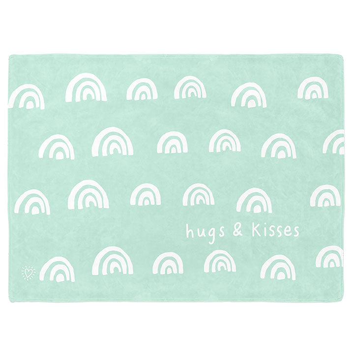 30 by 40 inch silky-soft fleece blanket that is hypoallergenic. Perfect size for a toddler or child. Bright white blanket printed on one side only. 4 rows of hand drawn rainbows in white with the words hugs & kisses hand drawn in white on a mint green background color. A small Adoptionly Yours heart logo by itself in white in lower left corner of blanket on front. 
