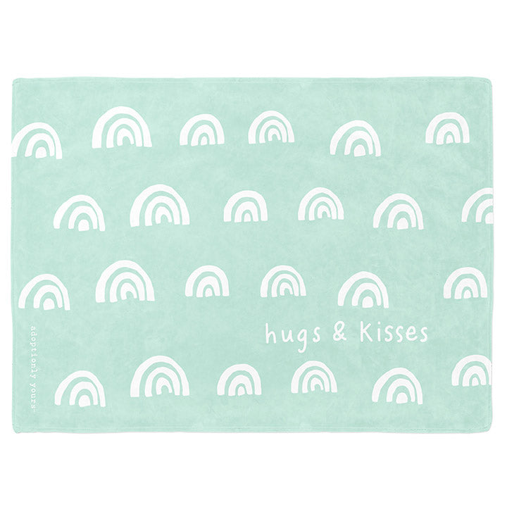 30 by 40 inch silky-soft fleece blanket that is hypoallergenic. Perfect size for a toddler or child. Bright white blanket printed on one side only. 4 rows of hand drawn rainbows in white with the words hugs & kisses hand drawn in white on a mint green background color. The words adoptionly yours in white typewriter font on lower left corner of blanket on front. 