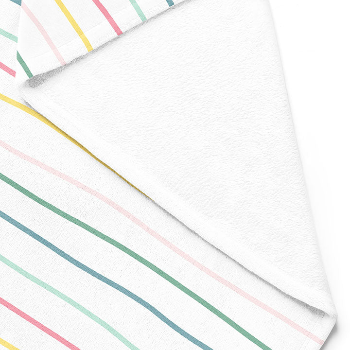 Backside of white 50 by 60 inch silky-soft fleece blanket that is hypoallergenic. Perfect size for an adult. Bright white blanket printed on one side only. 13 colorful hand drawn stripes of pink, green, blue, light teal, magenta and bright yellow run horizontally with the words xoxo, always in typewriter font. Adoptionly Yours heart logo by itself in pink in lower left corner of blanket on front. 
