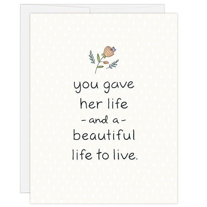 4.25 x 5.5 inch adoption greeting card for honoring birth parent of a girl. Blank inside. Simple and charming illustration style. Cream background with small salmon colored flower above title. Title You Gave Her Life and a Beautiful Life to Live.
