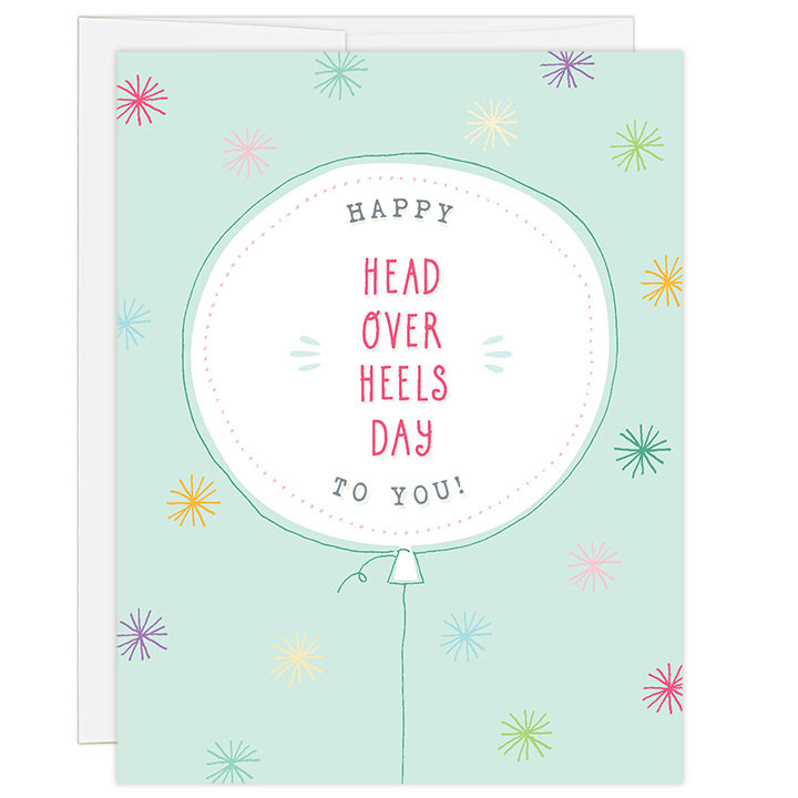 4.25 x 5.5 inch adoption celebration greeting card. Blank inside. Simple and charming illustration style. Title Happy Head Over Heels Day To You! Main image is a balloon holding the words to the title. Background is light green with brightly colored stars. 