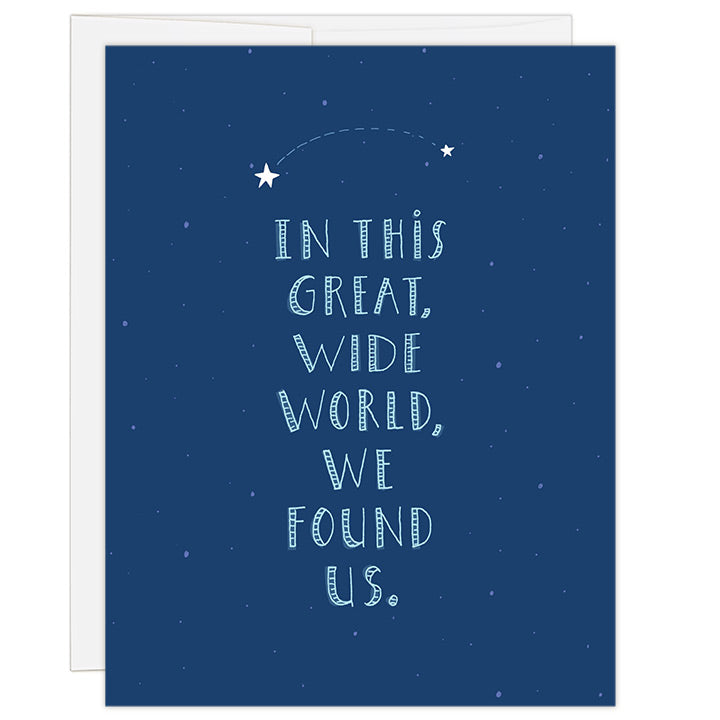 4.25 x 5.5 inch greeting card. Blank inside. Simple and charming illustration style. Title In This Great Wide World, We Found Us. Title is light teal color and is large and fills entire card. Above title are two white stars connected by a dashed line. Background is a deep blue color with lighter blue stars.