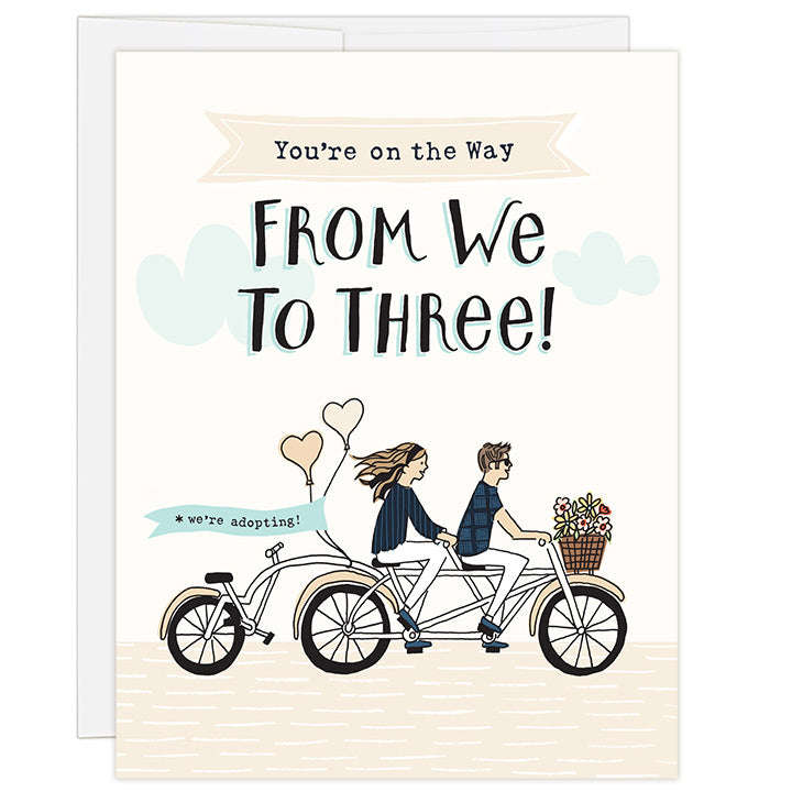 4.25 x 5.5 inch greeting card. Blank inside. Simple and charming illustration style. Title You’re on the Way From We to Three! Sub title *we’re adopting! Main image is a man and woman on a tandem bicycle and back seat is empty. There are flowers in the basket and balloons on the back with the words we’re adopting!