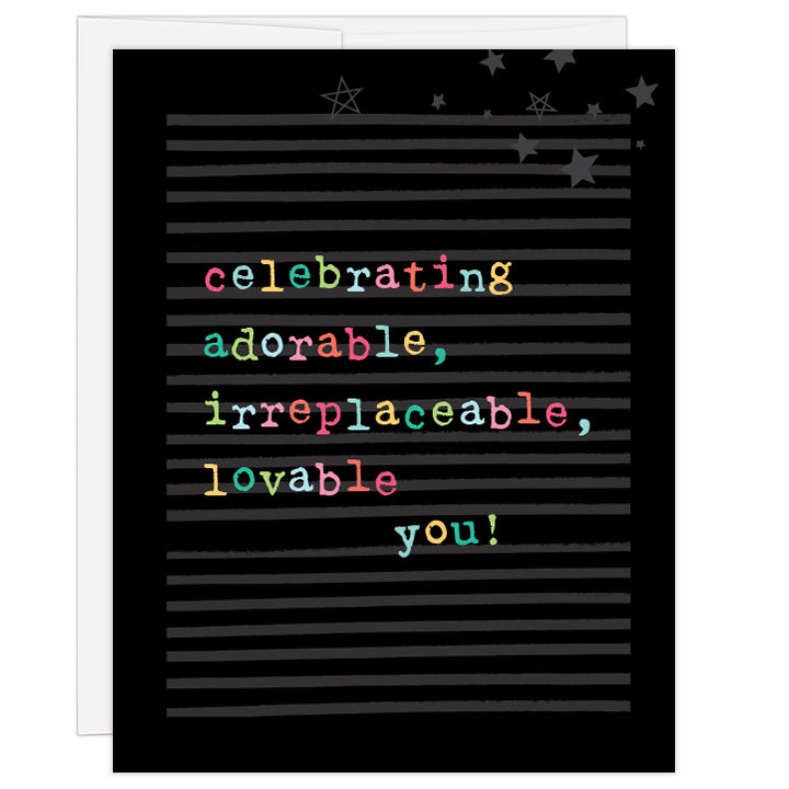 4.25 x 5.5 inch greeting card. Blank inside.  Cover is black and gray striped background with neon-coloring typewriter style letters and a sprinkle of stars. Text reads: celebrating adorable, irreplaceable, lovable you!