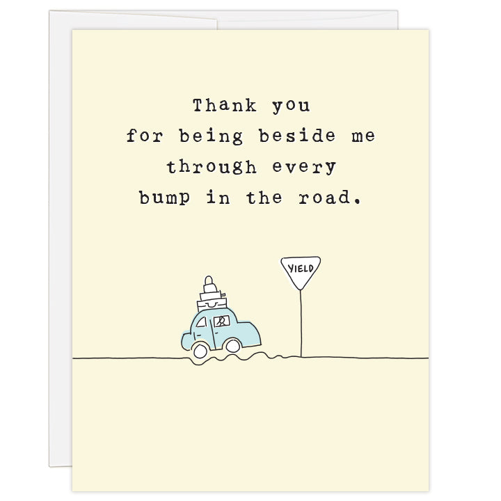 4.25 x 5.5 inch gratitude card for expressing thanks along the adoption journey. Blank inside. Artfully simplistic line drawing of a blue, luggage-laden car driving along a bumpy road and coming to a yield sign. Pale yellow background. Typewriter text reads: Thank you for being beside me through every bump in the road.