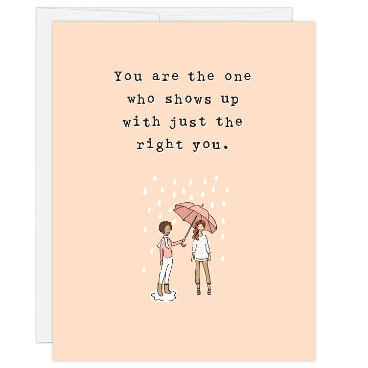 4.25 x 5.5 inch greeting card. Blank inside. Cover features charming line illustration of a woman holding an umbrella over another woman in the rain. Stylishly dressed women in shades of brown and salmon all against a pale peach background. Typewriter text reads: You are the one who shows up with just the right you.