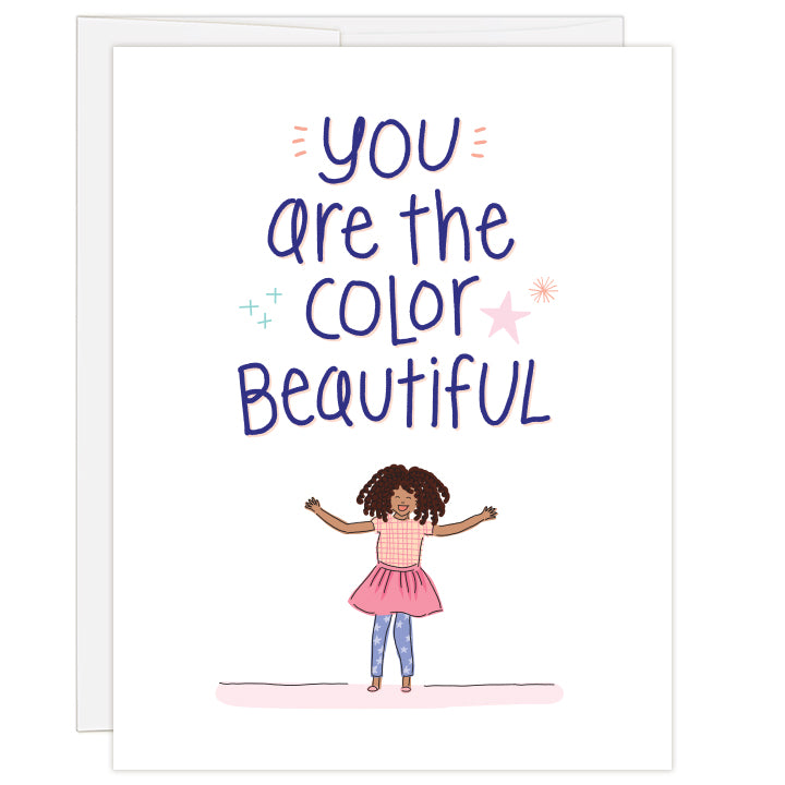 4.25 x 5.5 inch greeting card. Blank inside. Cover features bold headline above adorable African American girl in pink skirt, plaid shirt and blue starry leggings. Text reads: you are the color beautiful.